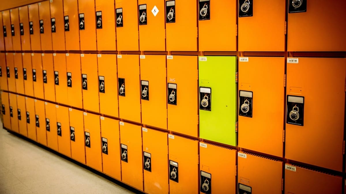 An empty school hallway lined with metal lockers and classroom doors under fluorescent lighting
